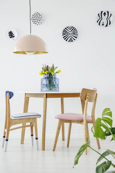 白い壁の模様のプレートとパステル調のダイニング ルームのインテリアのテーブルでピンクとブルーの木製椅子 — ストック写真