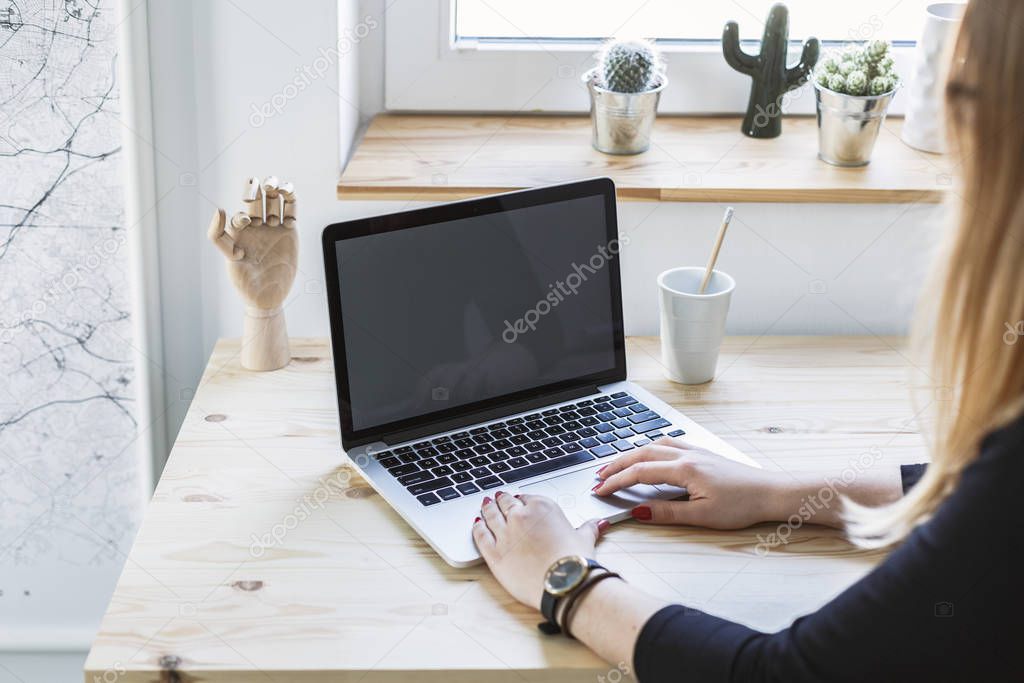 Woman typing on laptop with mockup screen by the wooden desk in home office interior