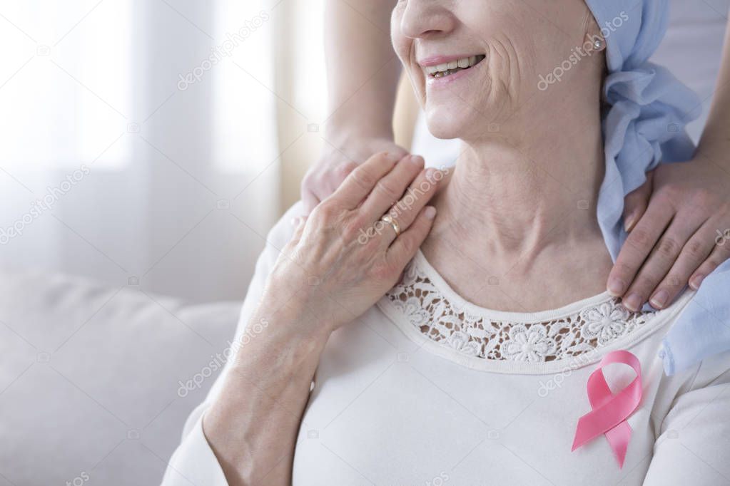 Close-up of smiling elderly woman with pink ribbon as symbol of fight against breast cancer