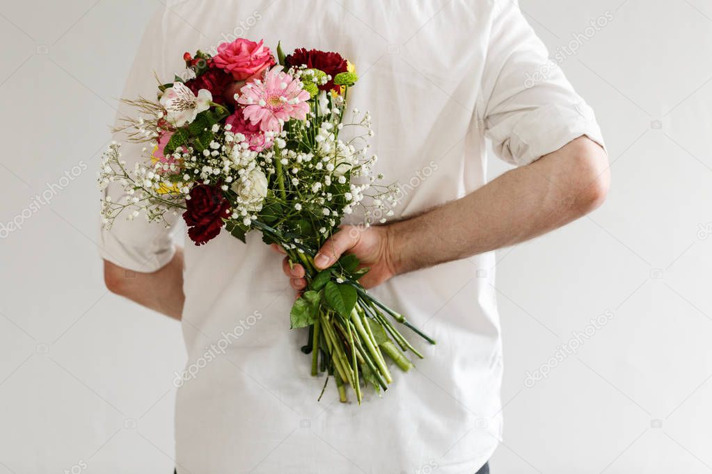 Man with bouquet of colorful flowers behind his back. Valentines day surprise concept