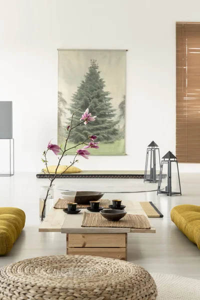 Close-up of a pouf in a living room interior with a coffee table, cherry blossom, lamps on the floor and a tree poster