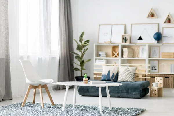 White coffee table with book and small decorative cactus and wooden chair standing on the carpet in Nordic style room interior with windows