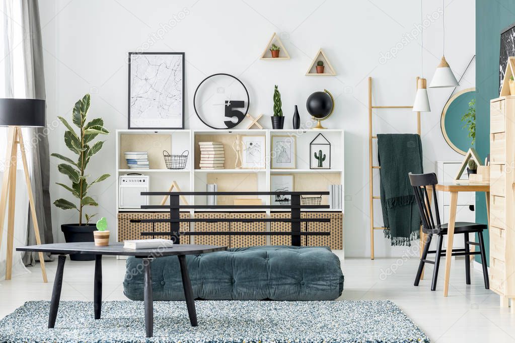 Black table on carpet near green futon in scandi living room interior with poster and ficus