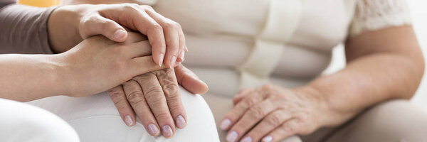 Close-up of person's hand supporting older and weak elderly woman