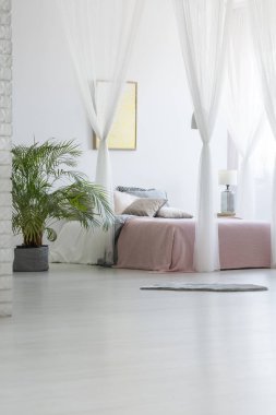Beyaz yatak odası iç yeşil bitki, modern poster duvar ve çift kişilik yatak Pembe battaniye ve yastık ile asılı ile katta yerleştirilen gri halı