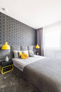 Gerçek fotoğraf gri yatak odası iç kral yatak, tuğla duvar, sarı lambalar ve el yapımı düğüm yastık