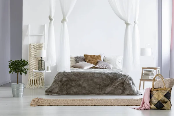 毛皮床罩放置在大床与垫子和树冠在白色卧室内部与地毯 稻草袋 枕头和毯子 新鲜的植物站在地板上和书籍在小桌子上 — 图库照片