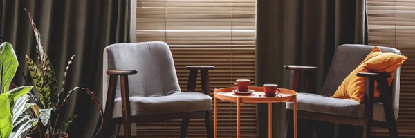 两个灰色的扶手椅 橙色的茶几和茶杯 客厅内有窗帘和窗帘的窗户 — 图库照片