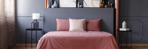 汚れたピンクのシートと金属のベッドサイド テーブルと灰色の寝室のインテリアに立って 壁に成形ダブル ベッドの枕 — ストック写真