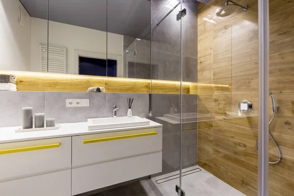 现代浴室内的木墙 上面有镜子 上面有黄色口音的白色柜子 — 图库照片