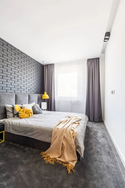 レンガの壁と窓でおおう灰色の寝室のインテリアでベッドの上の黄色の毛布 — ストック写真