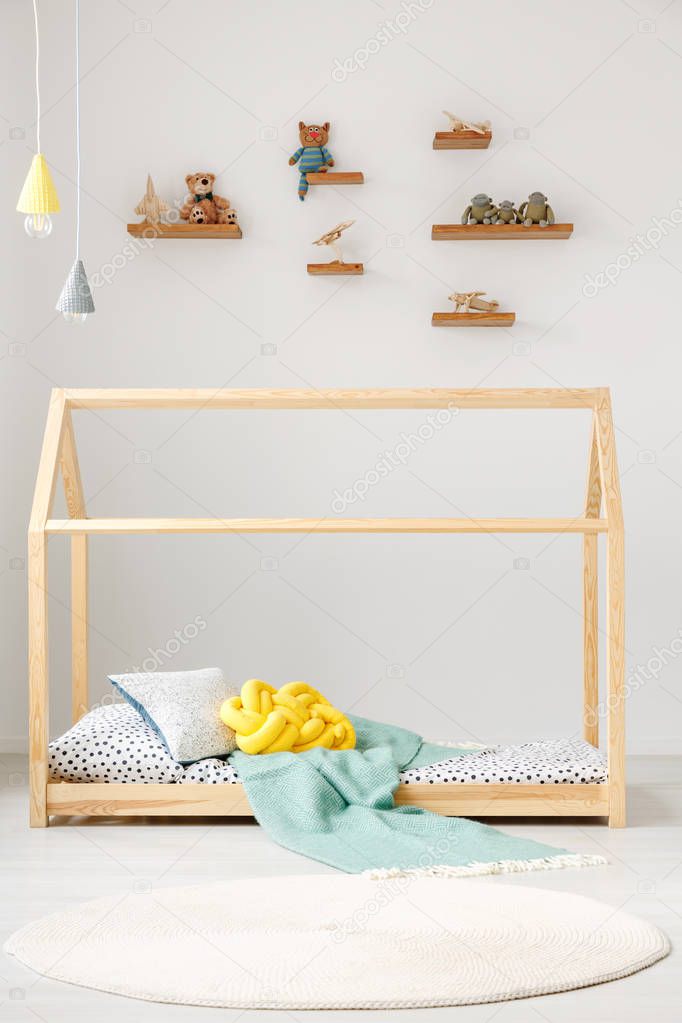 Child toys on shelves on a white wall and a wooden house bed frame for a toddler in a cute bedroom interior