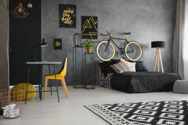 Modern gencin yatak odası iç yatak başı, sarı sandalye, Masa ve ahşap lamba bisikletle ile ham, gri duvara siyah yatak duran gerçek fotoğraf