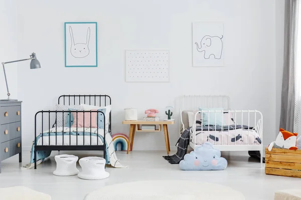 stock image Cozy bedroom interior for brother and sister. Two beds, white and black with bedding and pillows, and a small table in between. Rabbit and elephant posters on the wall. Real photo