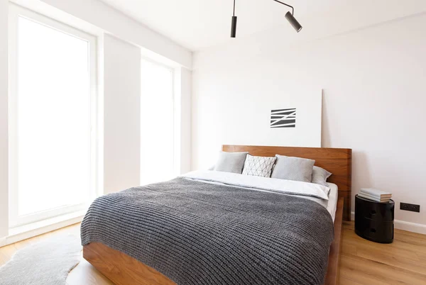 灰色毯子在木床在白色明亮的卧室内部与简单的海报 真实照片 — 图库照片