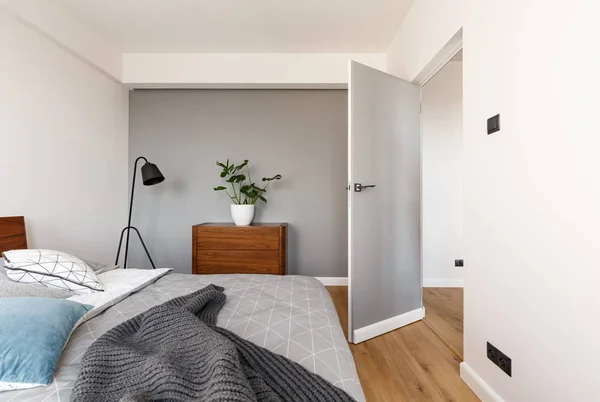 木製キャビネットのドアの近くに工場を持つ最小限の寝室のインテリアでベッドの上灰色のブランケット 実際の写真 — ストック写真