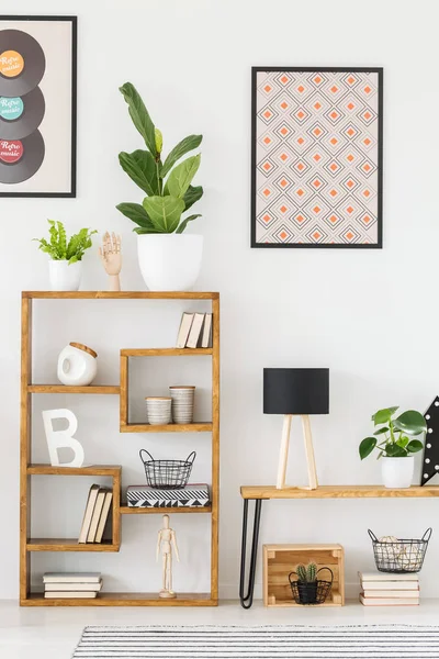 Real photo of a wooden shelf with ornaments in a living room with posters on the wall