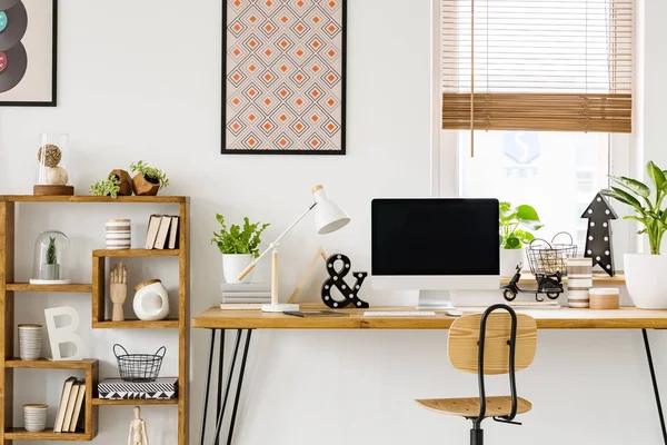 真实照片的办公桌与电脑屏幕 灯和装饰品站在一个椅子旁边的一个架子上 墙上的海报和窗帘的窗口 — 图库照片