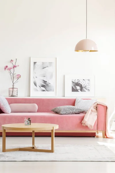 Настоящее Фото Розового Дивана Подушками Стоящими Столом Перед Полкой Плакатами — стоковое фото