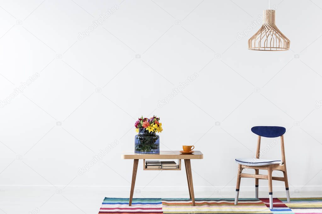 Gold lamp above wooden chair next to table with flowers in folk dining room interior