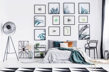 Bir sandalye ve bir raf, lamba ve de bir ferah yatak odası iç üçgen kilim ve duvar resimleri, tam ile bir saat arasında geniş yatak duran gerçek fotoğraf