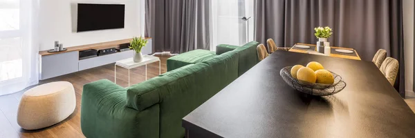 Apartment interior with a green sofa, pouf, cabinet, tv on the wall, kitchen island and dinning table