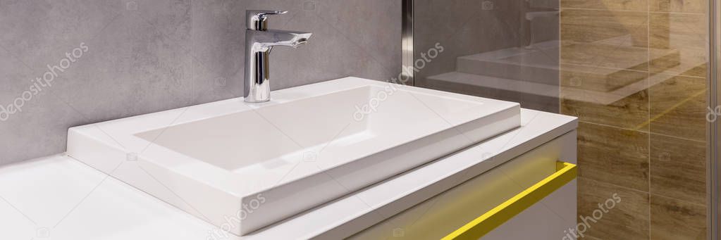 Close-up of a ceramic washbasin with a faucet and yellow handle in bathroom interior