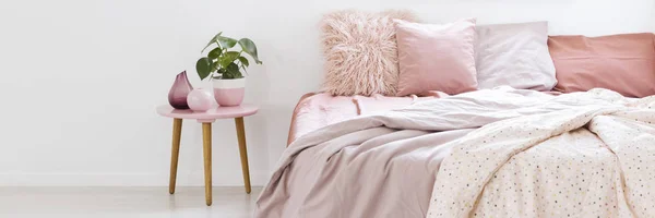 寝室のインテリアと白い壁にピンクの寝具が付いているベッドの横にある工場の地位と小さなテーブルの実際の写真 — ストック写真