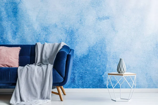 モダンなリビング ルームのインテリアで青と白のオンブル壁に毛布と枕が付いている暗いソファー横の花瓶と現代的な透かし彫り金属サイド テーブル 実際の写真 — ストック写真