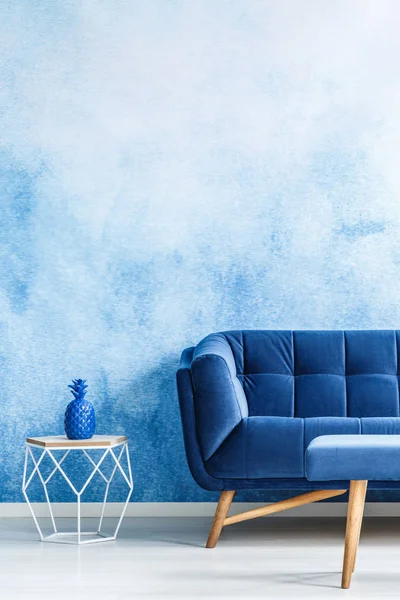 Copy space monochromatic living room interior with plush, navy blue couch and metal side table against ombre wall. Real photo.