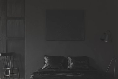 Mockup of black empty poster above bed in dark bedroom interior with chair. Real photo clipart