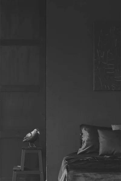 Sculpture on stool next to bed in black bedroom interior with decor on the wall. Real photo