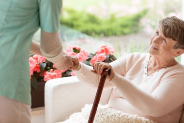 Parkinson hastalığı ile yaşlı bir kadın yardım Doktor rehabilitasyon tesisinde bir kanepe kalkmak