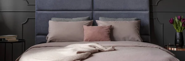 毛布とダブルベッド つのベッドサイド テーブル本と紫のチューリップと暗い寝室のインテリアで立って汚いピンクのシート — ストック写真