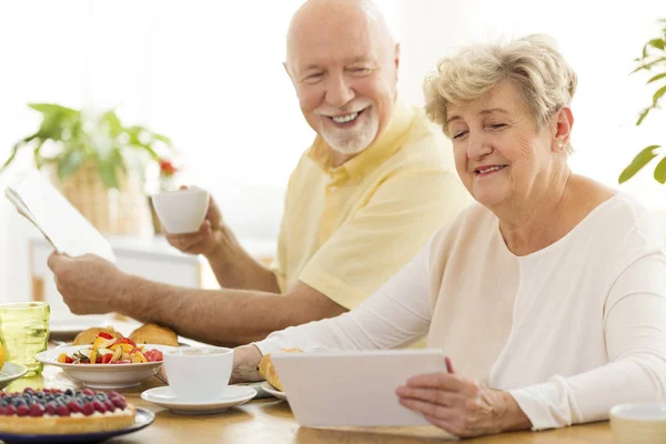 愉快的祖父喝茶和祖母用片剂在早餐期间 — 图库照片
