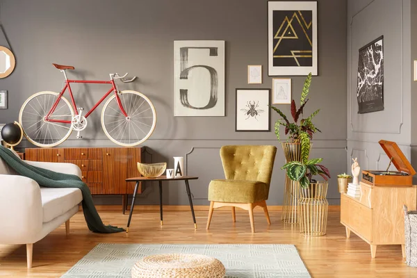 Unique vintage living room interior with homey feeling, mixture of old-fashioned furniture and objects, armchair, gramophone and sketches on a gray wall