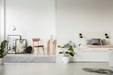 Bir platform bed ayakta bir sandalye, küçük masa, posterler ve ferah yatak odası iç bir ampul yanında gerçek fotoğraf