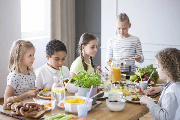 私立の小学校で 昼食時に食堂内のテーブルが健康的な食事を楽しむ子どもたちを破る — ストック写真