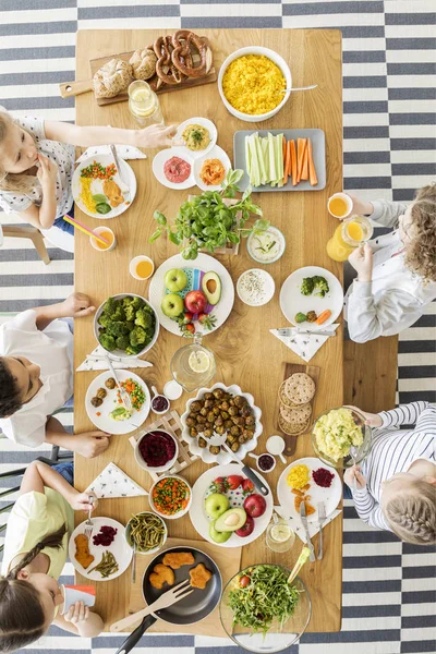 Wooden table top with colorful vegetables, fruit, cooked dishes. Children eating their healthy meal during a lunch break at a private primary school. Top view.