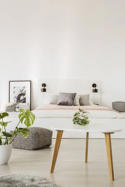 植物旁边的白色表在卧室内部与复制空间以上的床和海报 真实照片 — 图库照片