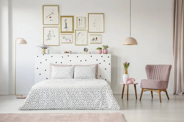 粉红色扶手椅旁边的花纹床在女性卧室内部与海报画廊 — 图库照片