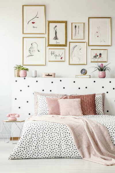 Pink blanket on patterned bed with headboard in woman's bedroom interior with posters
