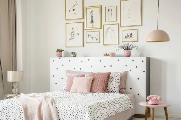 Beautiful white bedroom interior with feminine decor, polka dot pattern, pink accessories and framed sketches gallery on the wall