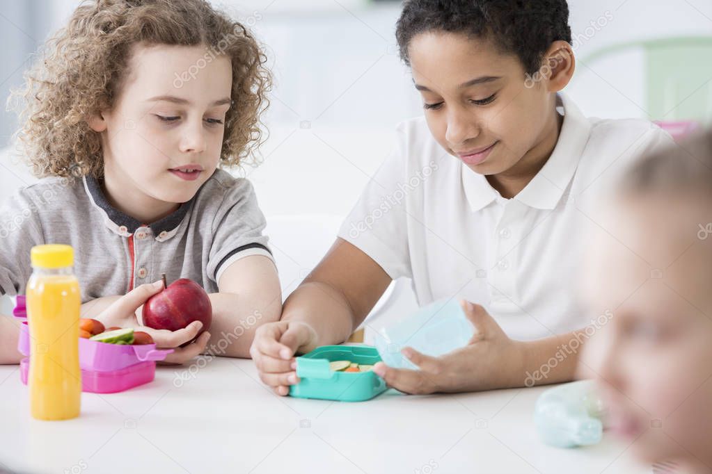 African-american boy and his friend eating an apple during break at school