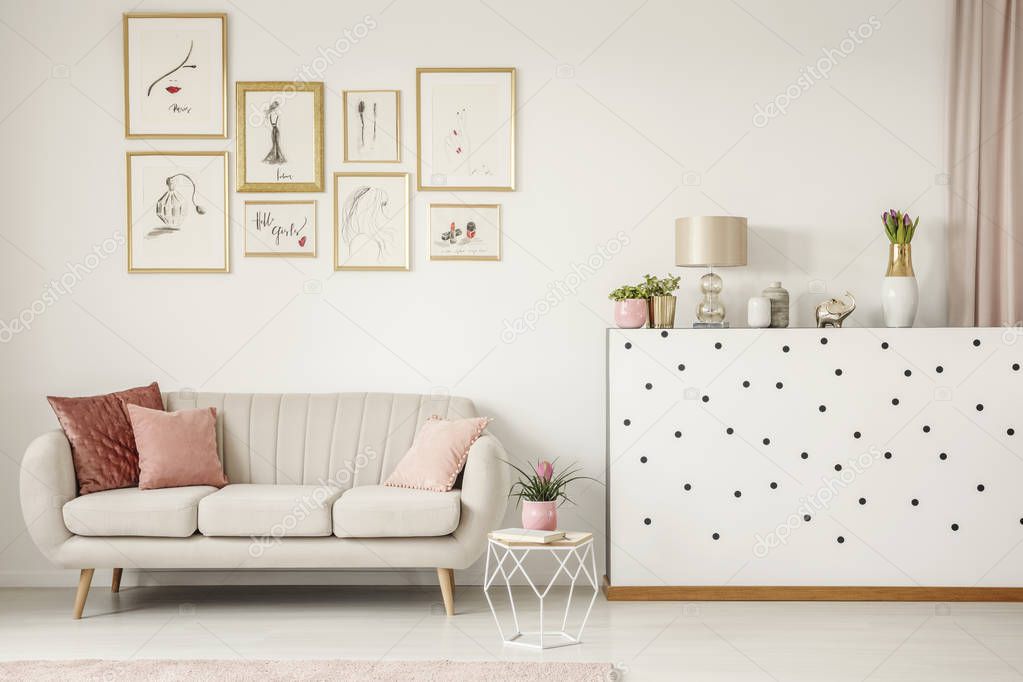 Pink pillow on beige sofa in feminine living room interior with plant and gallery of posters
