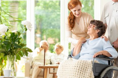 Yaşlı bir adam tekerlekli bir bakım tesisi için veda ihale caregiver. Tekerlekli sandalye iterek bir arkadaşı. Arka plan bulanık başka yaşlı insanlarda.