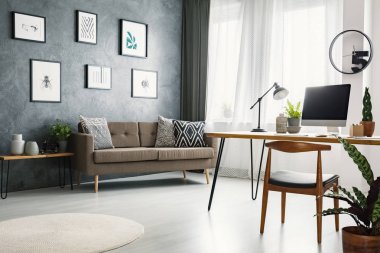 Uzaktan çalışma köşe masası yaşayan posterler ile ham Duvar ile iç oda, yastıklar ve pencere perdeleri ile kanepe