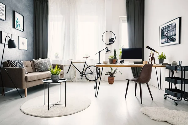 黑色椅子在木桌与台式计算机在工作区内部与沙发和自行车 真实照片 — 图库照片