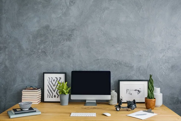 Plants, posters and desktop computer on desk in grey home office interior with copy space. Real photo