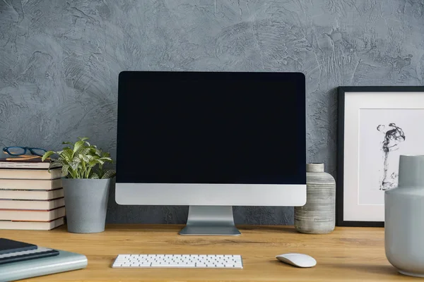 Mockup of desktop computer on wooden desk with plant in grey workspace interior. Real photo
